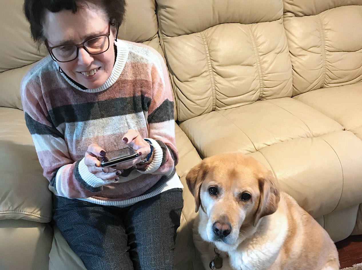 Julie sitting on the couch, iPhone in her hand, with her dog Winston.