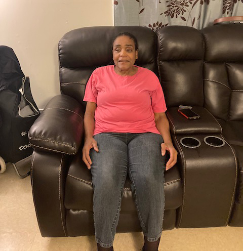 Mary Conner sitting on her couch, wearing a bright pink shirt and jeans.