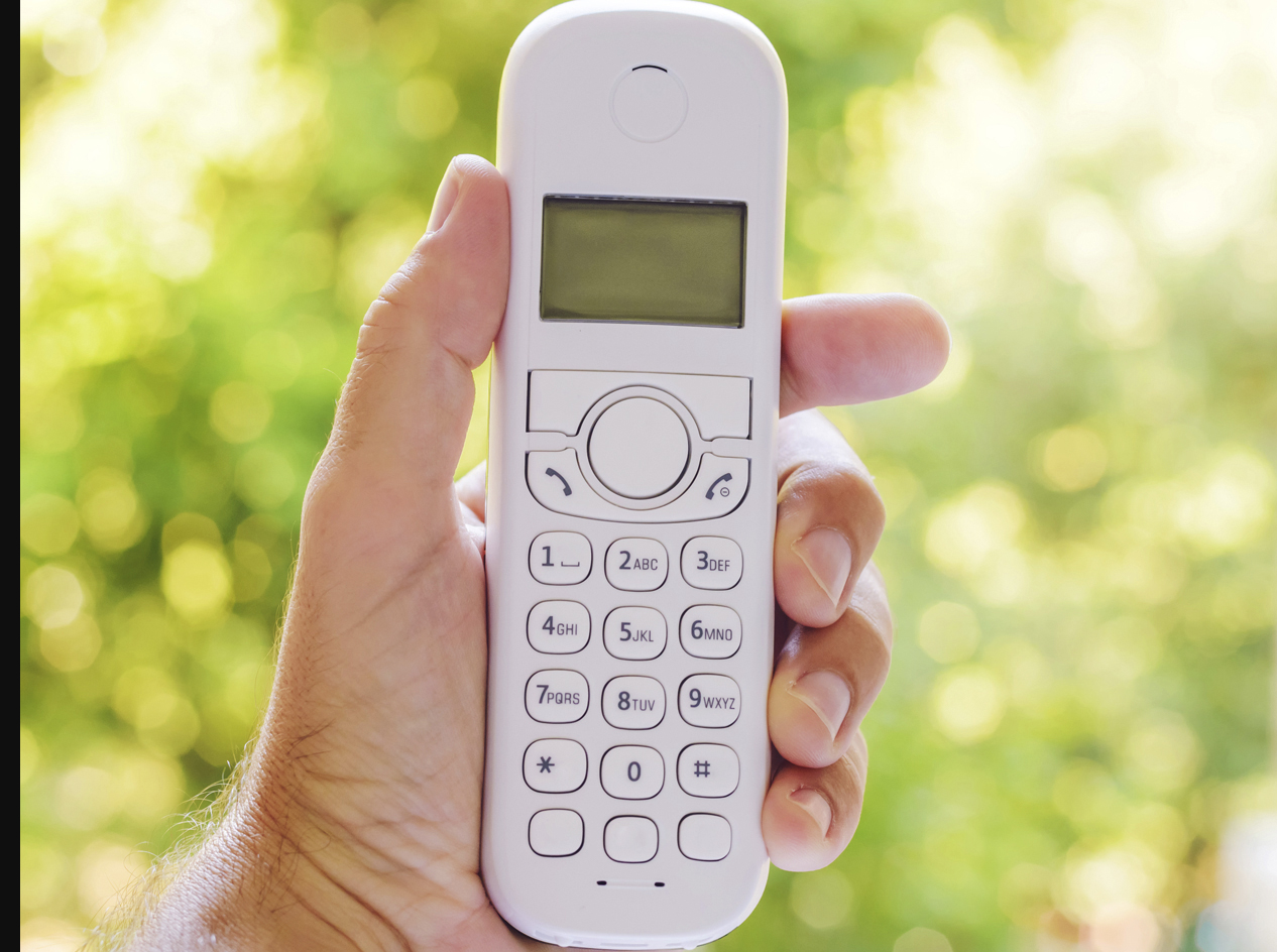 Hand holding a white cordless telephone with buttons.