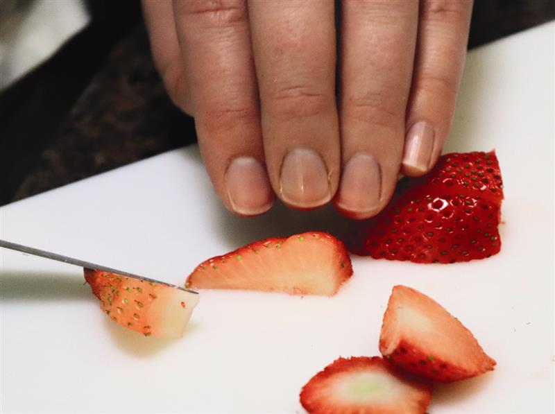 Hand holding strawberry pieces on white cutting board after having sliced them