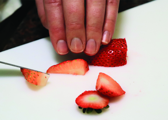 Hand holding strawberry pieces on white cutting board after having sliced them