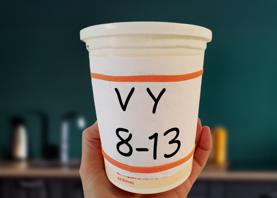 Hand holding large yogurt container with a large print label: V-Y and 8-13