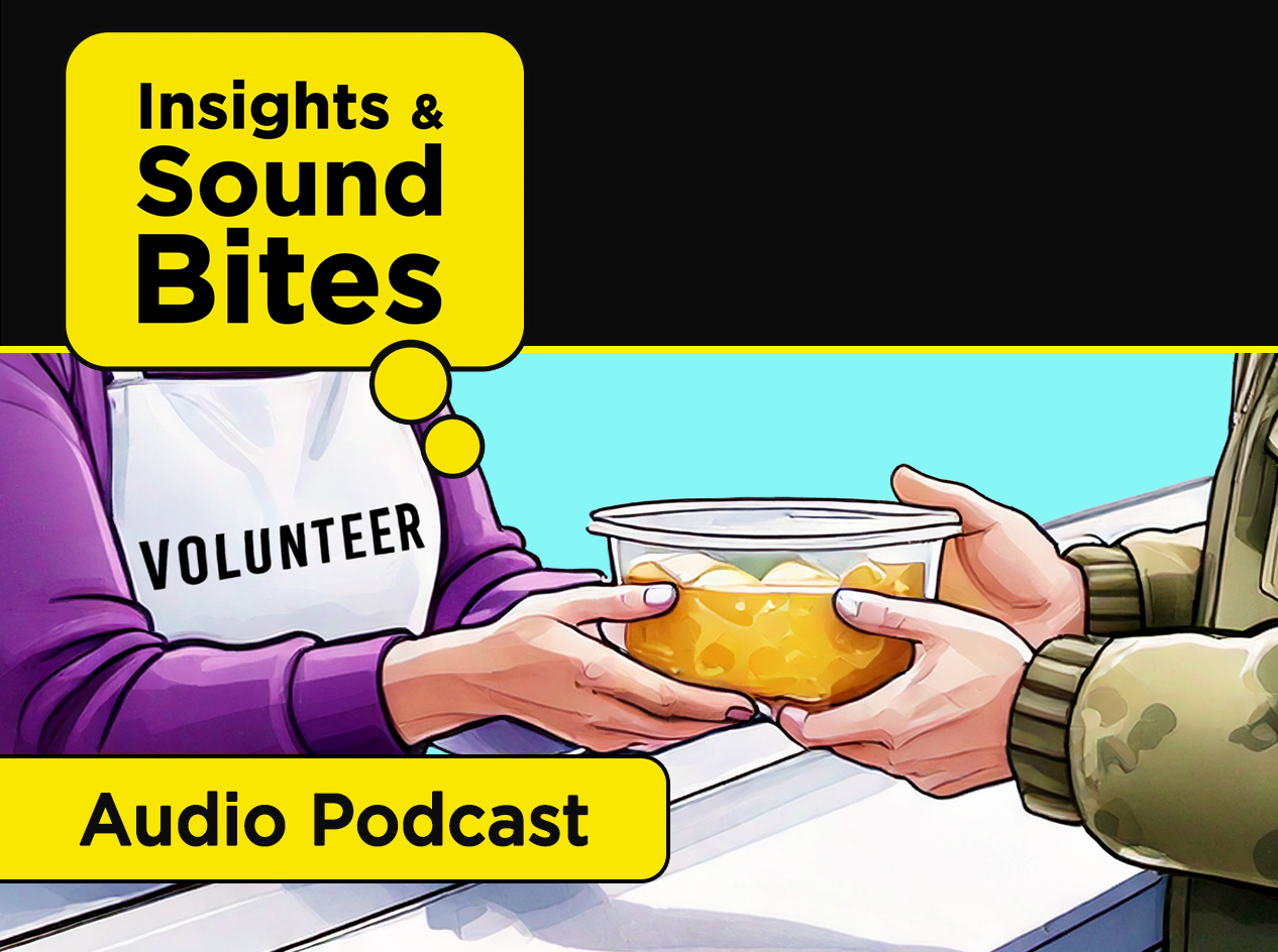 A woman wearing a white apron, with the word Volunteer in black, hands a container of soup to a man in a camouflage jacket.