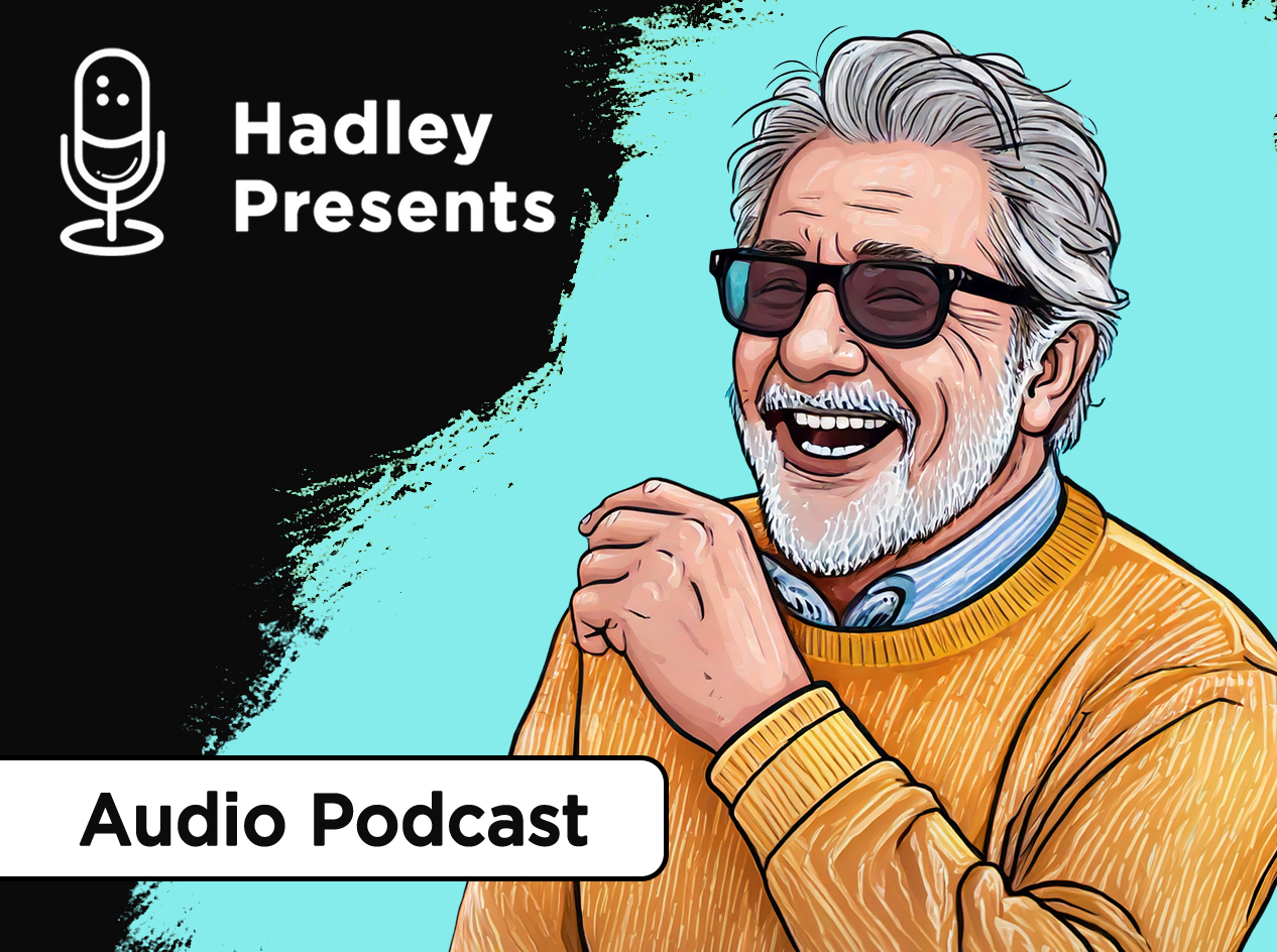 Older man with salt-and-pepper hair, beard, and mustache, wearing dark glasses and an orange sweater and laughing heartily.