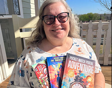 Mary Myers, a Hadley member with macular degeneration, smiling and holding several of her award-winning children's books