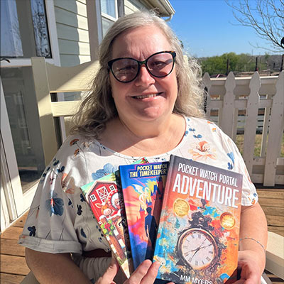 Mary Myers, a Hadley member with macular degeneration, smiling and holding several of her award-winning children's books