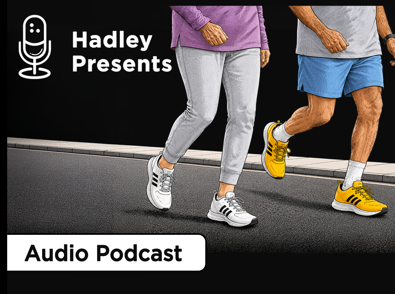 An older woman walking and an older man jogging together on a road beside a sidewalk, both wearing athletic clothing and sneakers.